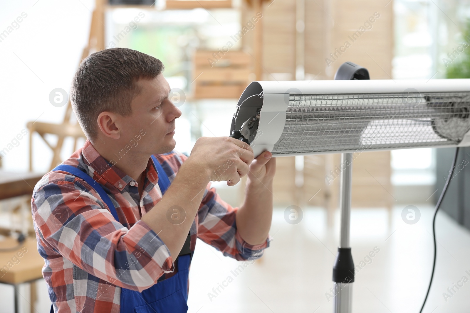 Photo of Professional technician repairing electric infrared heater with pliers indoors