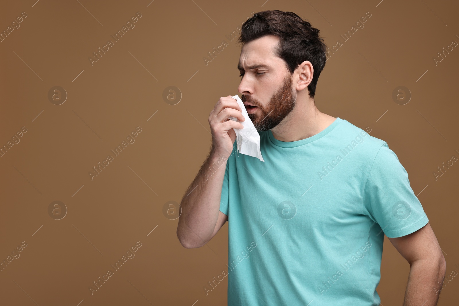 Photo of Sick man with tissue coughing on brown background, space for text