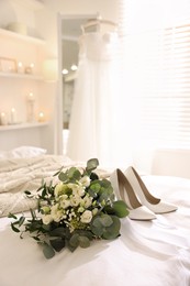 Photo of Beautiful wedding bouquet and bride's shoes on bed in room
