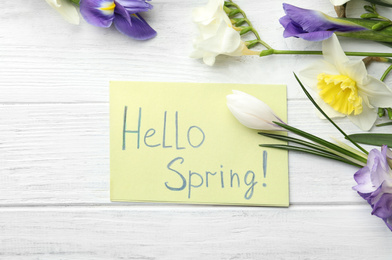 Photo of Card with words HELLO SPRING and fresh flowers on white wooden table, flat lay