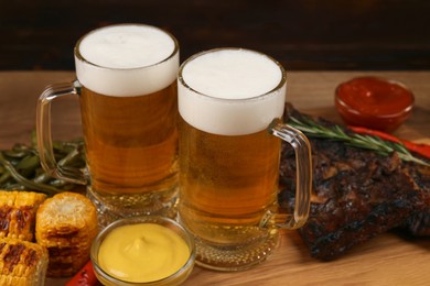 Mugs with beer, delicious grilled ribs and ingredients on wooden table