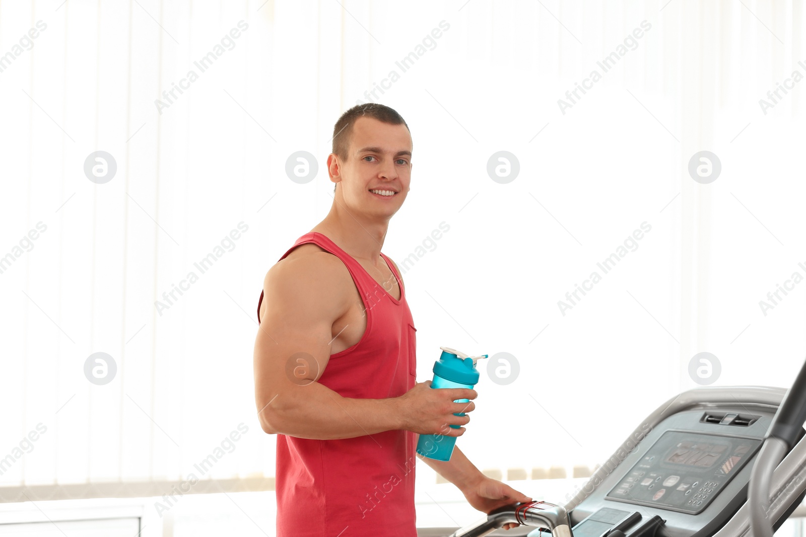 Photo of Athletic young man with protein shake on running machine in gym