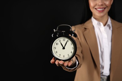 Photo of Businesswoman holding alarm clock on black background, closeup with space for text. Time management