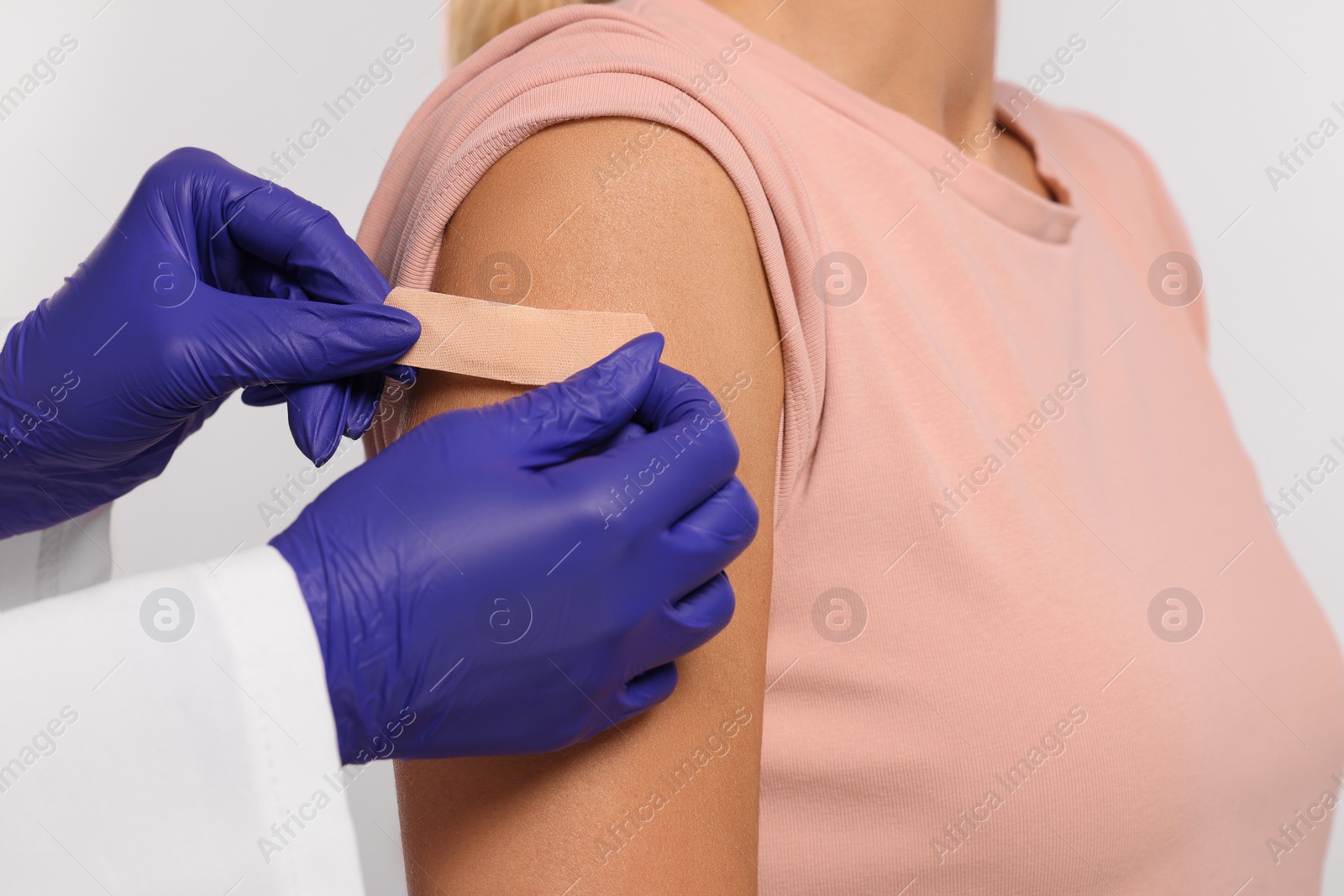 Photo of Nurse sticking adhesive bandage on woman's arm after vaccination on light background, closeup