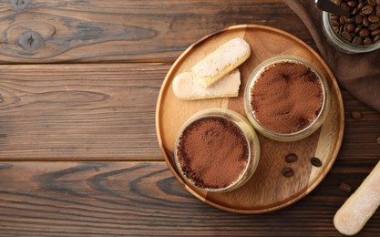 Photo of Delicious tiramisu in glasses, coffee beans and cookies on wooden table, flat lay. Space for text