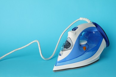 Photo of One modern iron on light blue background, space for text. Home appliance