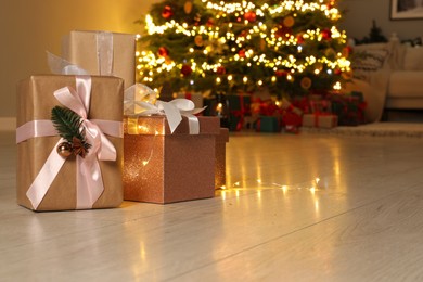 Beautiful gift boxes against fir tree with Christmas lights indoors, space for text