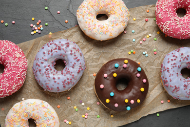 Photo of Yummy donuts with sprinkles on dark background, flat lay