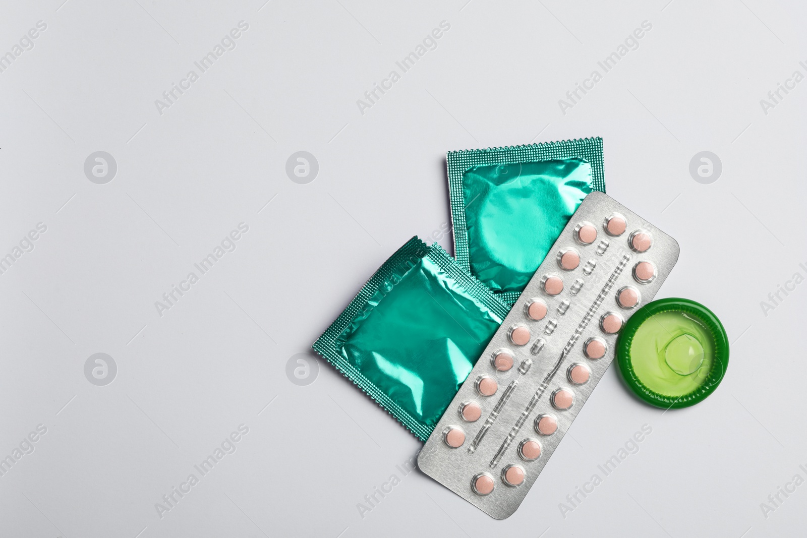 Photo of Condoms and birth control pills on light grey background, flat lay with space for text. Safe sex concept