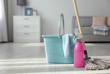 Photo of Bucket, mop and bottle of cleaning product on floor indoors. Space for text