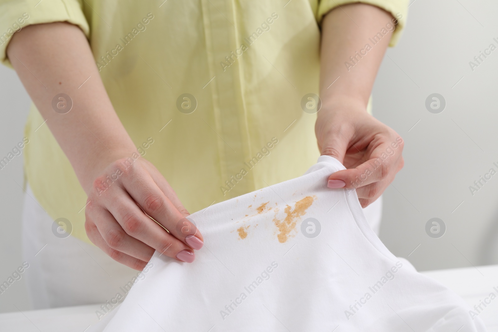 Photo of Woman holding shirt with stain at table against light grey background, closeup