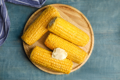 Delicious boiled corn with butter on light blue wooden table, flat lay