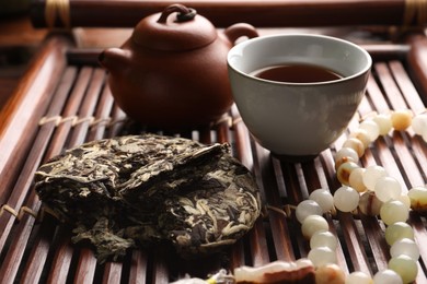 Photo of Aromatic pu-erh tea and prayer beads on wooden tray, closeup. Traditional ceremony