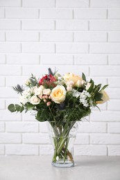 Photo of Beautiful bouquet with roses on grey table against white brick wall
