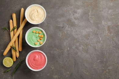 Different kinds of tasty hummus served with bread sticks on grey table, flat lay. Space for text