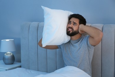 Photo of Unhappy young man covering ears in bed at home. Noisy neighbours