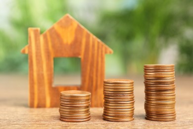 Photo of Mortgage concept. House model and stacks of coins on wooden table against blurred green background