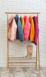 Photo of Wooden rack with warm jackets near white brick wall