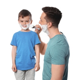 Dad applying shaving foam onto son's face against white background