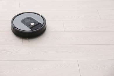 Photo of Modern robotic vacuum cleaner on wooden floor. Space for text