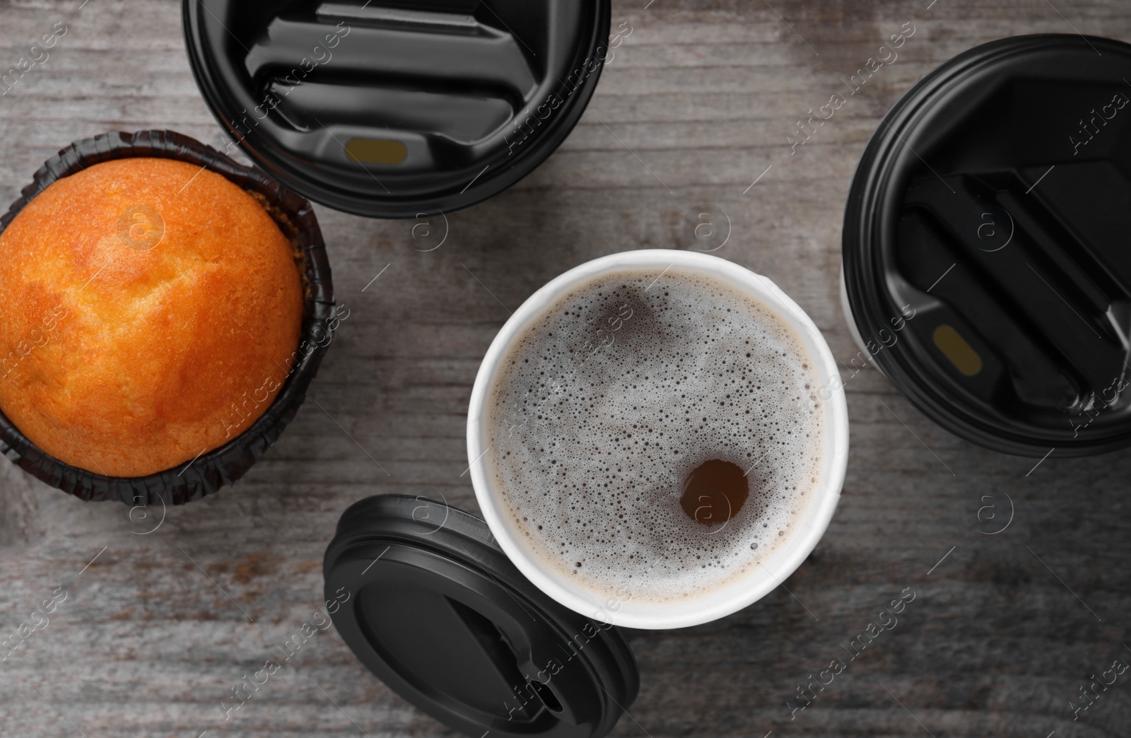 Photo of Coffee to go. Paper cups with tasty drink and muffin on wooden table, flat lay