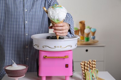 Photo of Woman holding waffle cone with cotton candy near machine, closeup. Making dessert