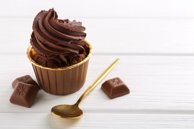 Delicious cupcake and chocolate pieces on white wooden table, closeup. Space for text