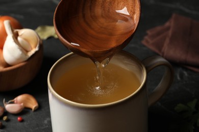 Pouring hot delicious bouillon into cup on black table, closeup