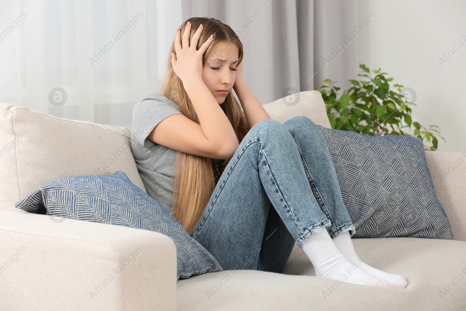 Photo of Depressed teenage girl sitting on sofa at home