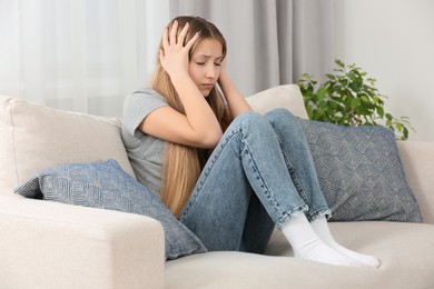 Depressed teenage girl sitting on sofa at home