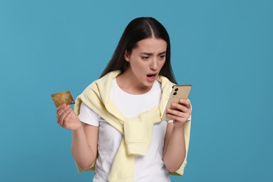 Photo of Shocked woman with credit card and smartphone on light blue background. Debt problem