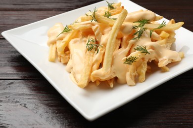 Delicious french fries with cheese sauce and dill on wooden table, closeup