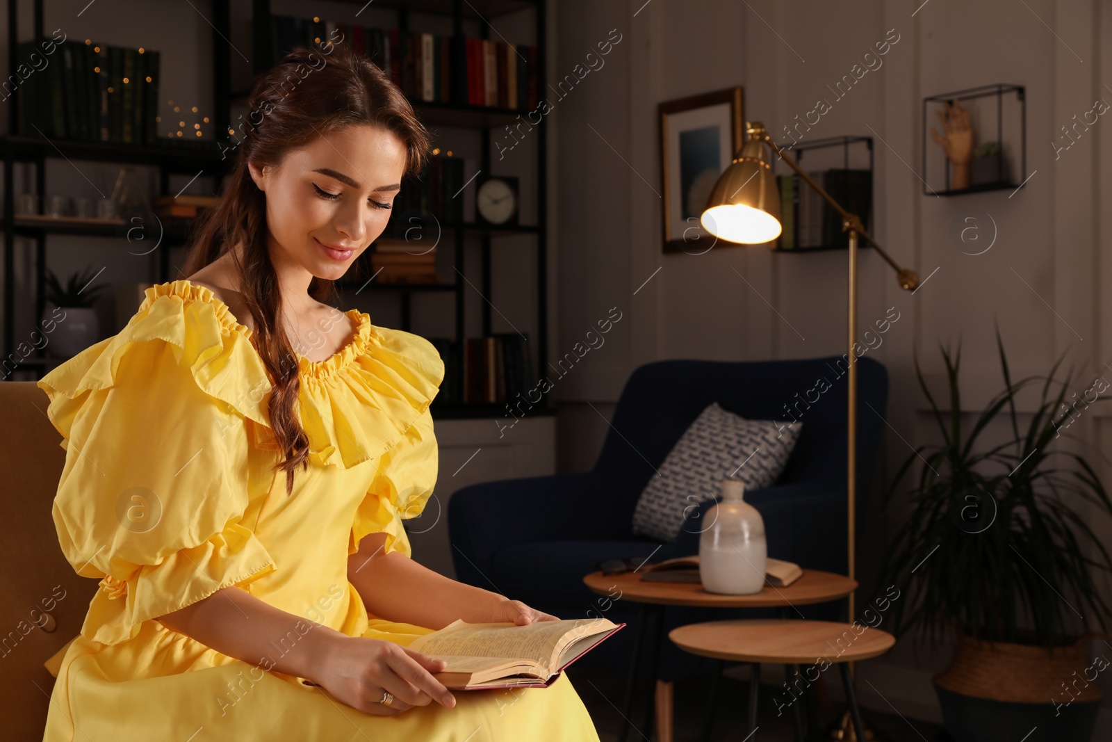 Photo of Beautiful young woman in yellow dress reading book at home