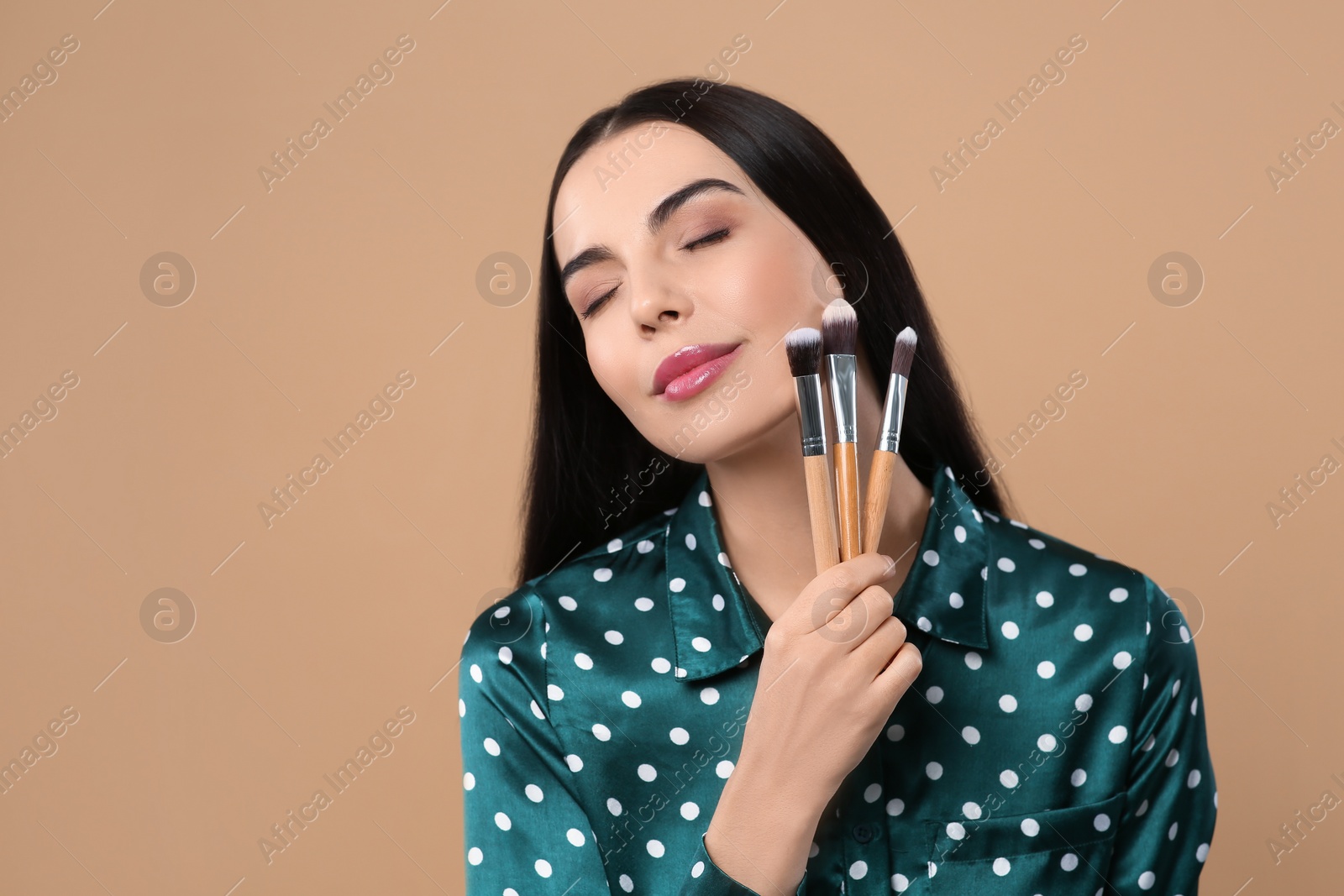 Photo of Beautiful woman with different makeup brushes on light brown background. Space for text