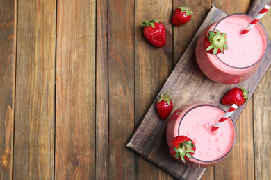 Photo of Tasty strawberry smoothies in glasses on wooden table, flat lay. Space for text