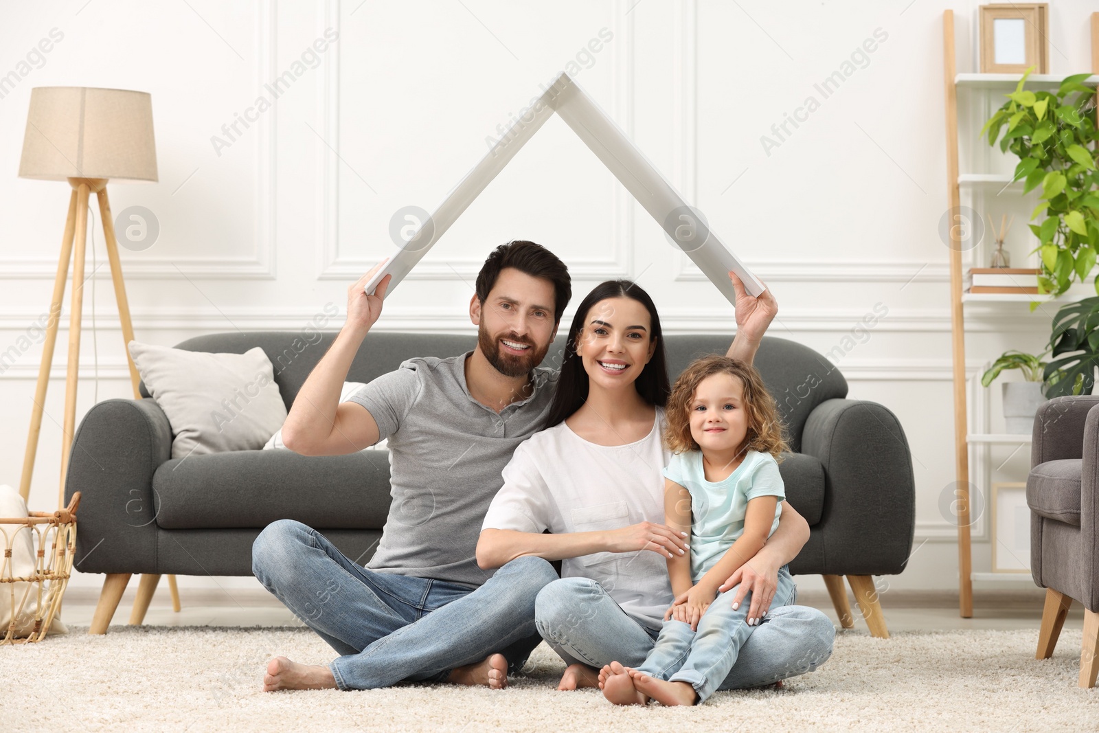 Photo of Housing concept. Happy husband holding plastic roof over his family while sitting on floor at home