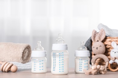 Photo of Feeding bottles with milk and baby accessories on wooden table indoors