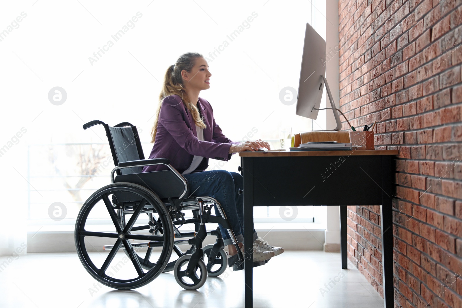 Photo of Woman in wheelchair working with computer at table indoors