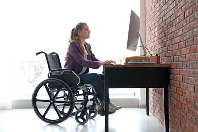 Woman in wheelchair working with computer at table indoors