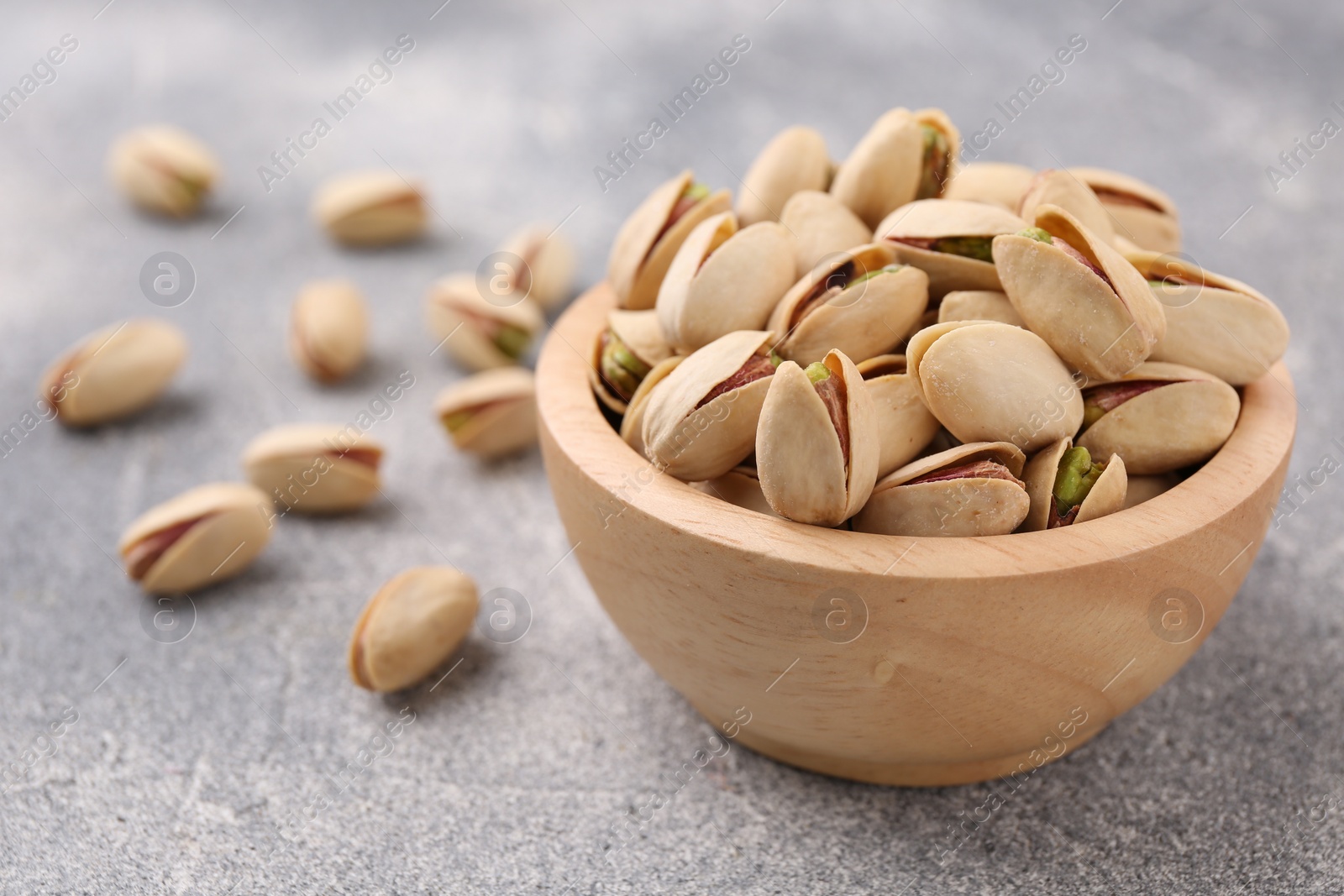 Photo of Delicious pistachios in bowl on grey textured table