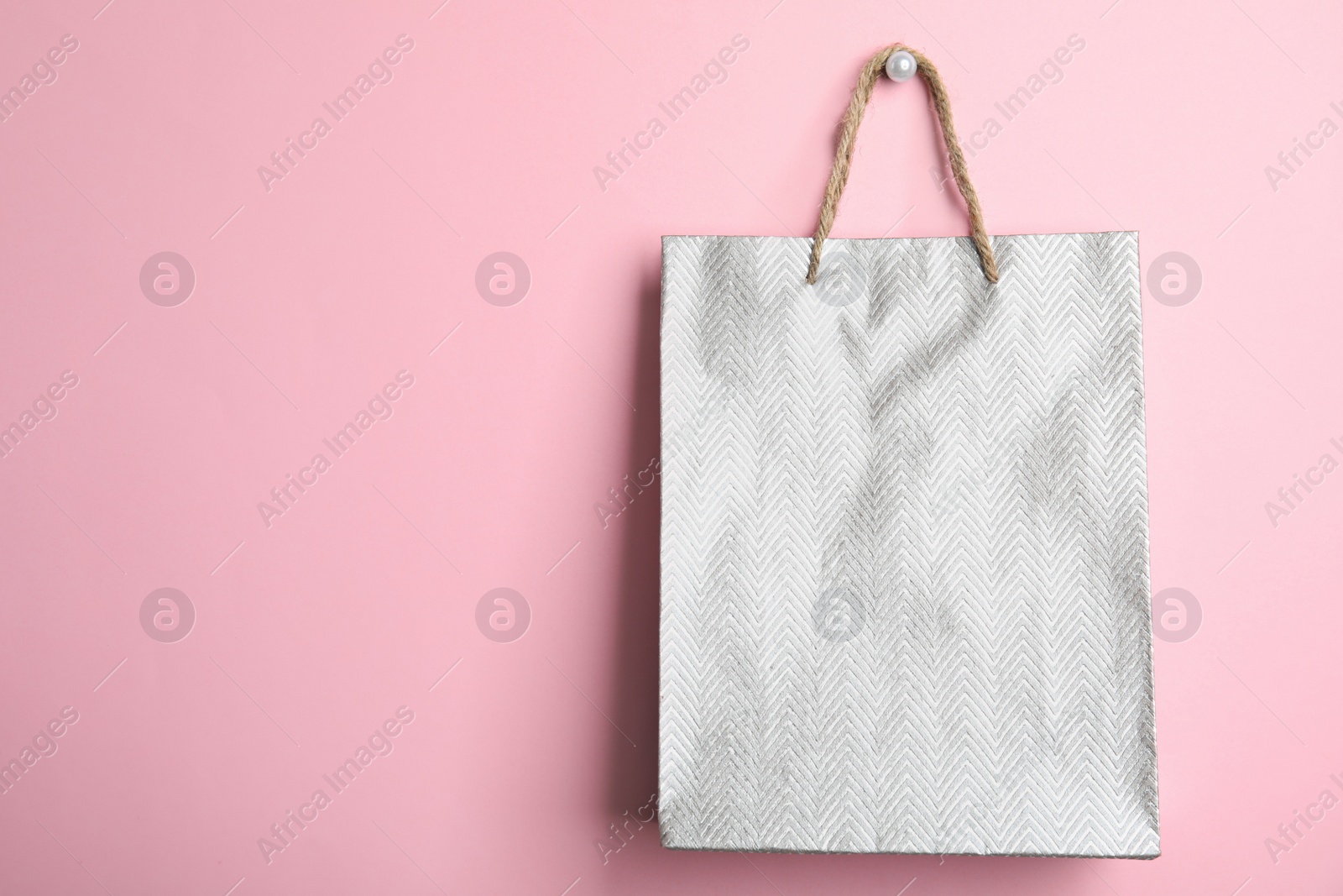 Photo of Silver shopping paper bag on pink background, space for text