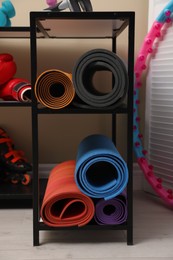 Photo of Different yoga mats on rack indoors. Sports equipment