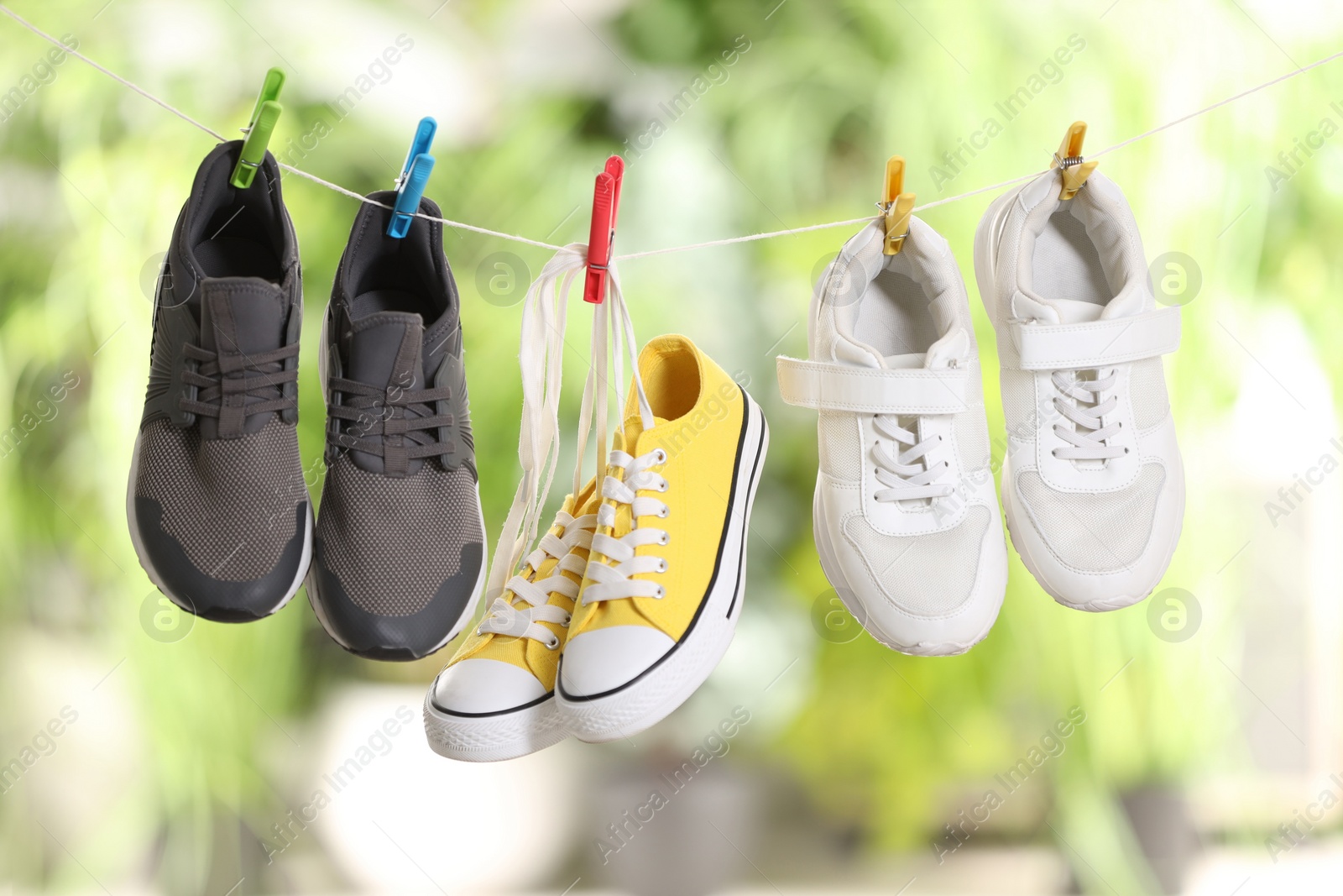 Photo of Different stylish sneakers drying on washing line against blurred background