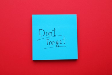 Photo of Paper note with phrase Don't Forget on red background, top view