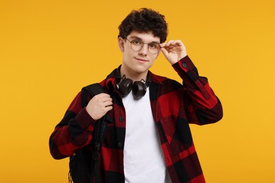 Photo of Portrait of student with backpack, headphones and glasses on orange background