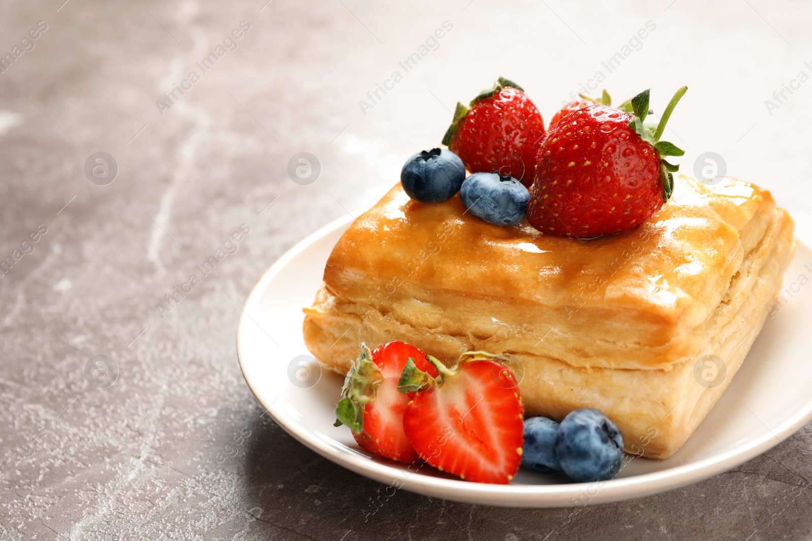 Photo of Fresh delicious puff pastry with sweet berries on grey marble table, closeup. Space for text