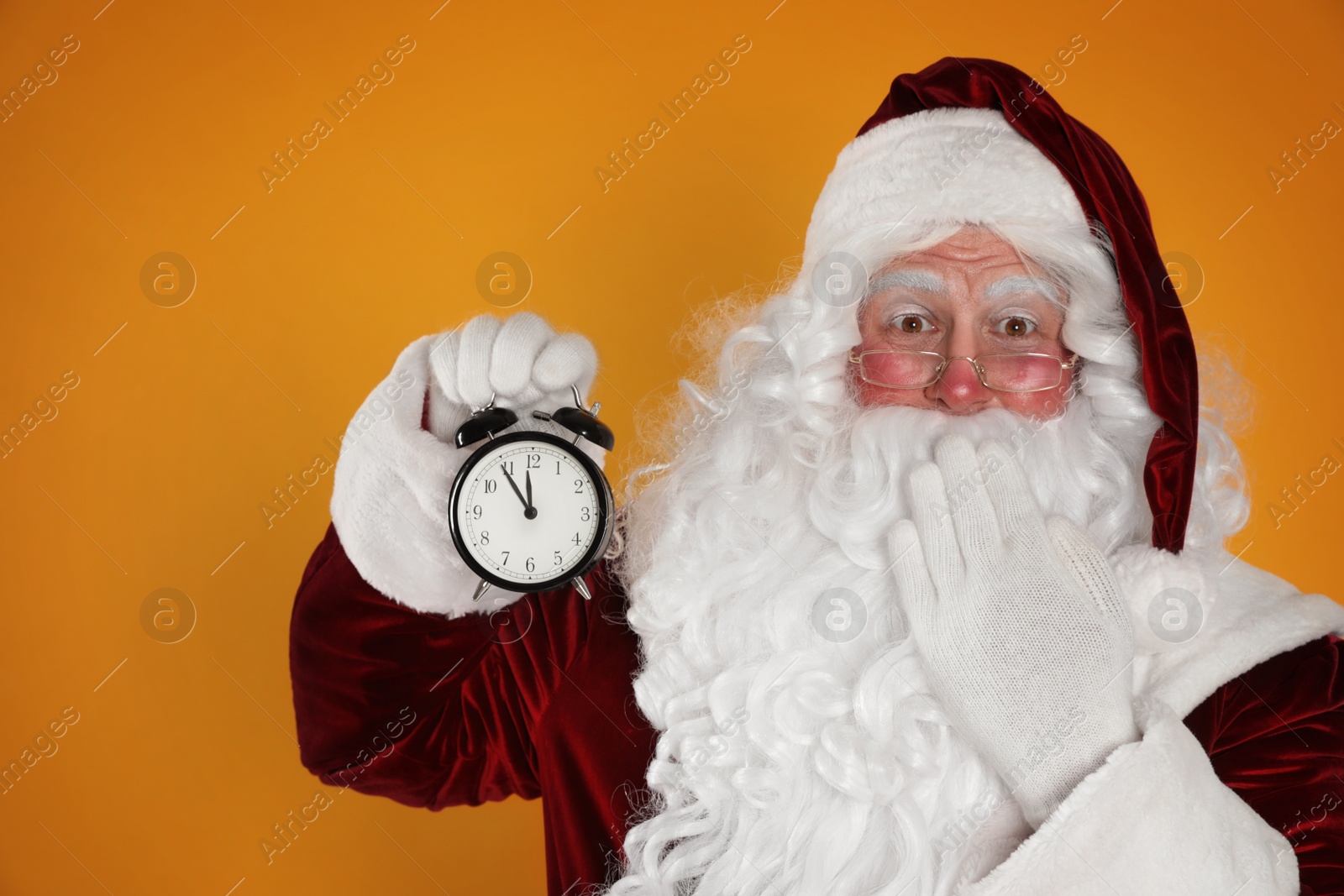 Photo of Santa Claus holding alarm clock on yellow background. Christmas countdown