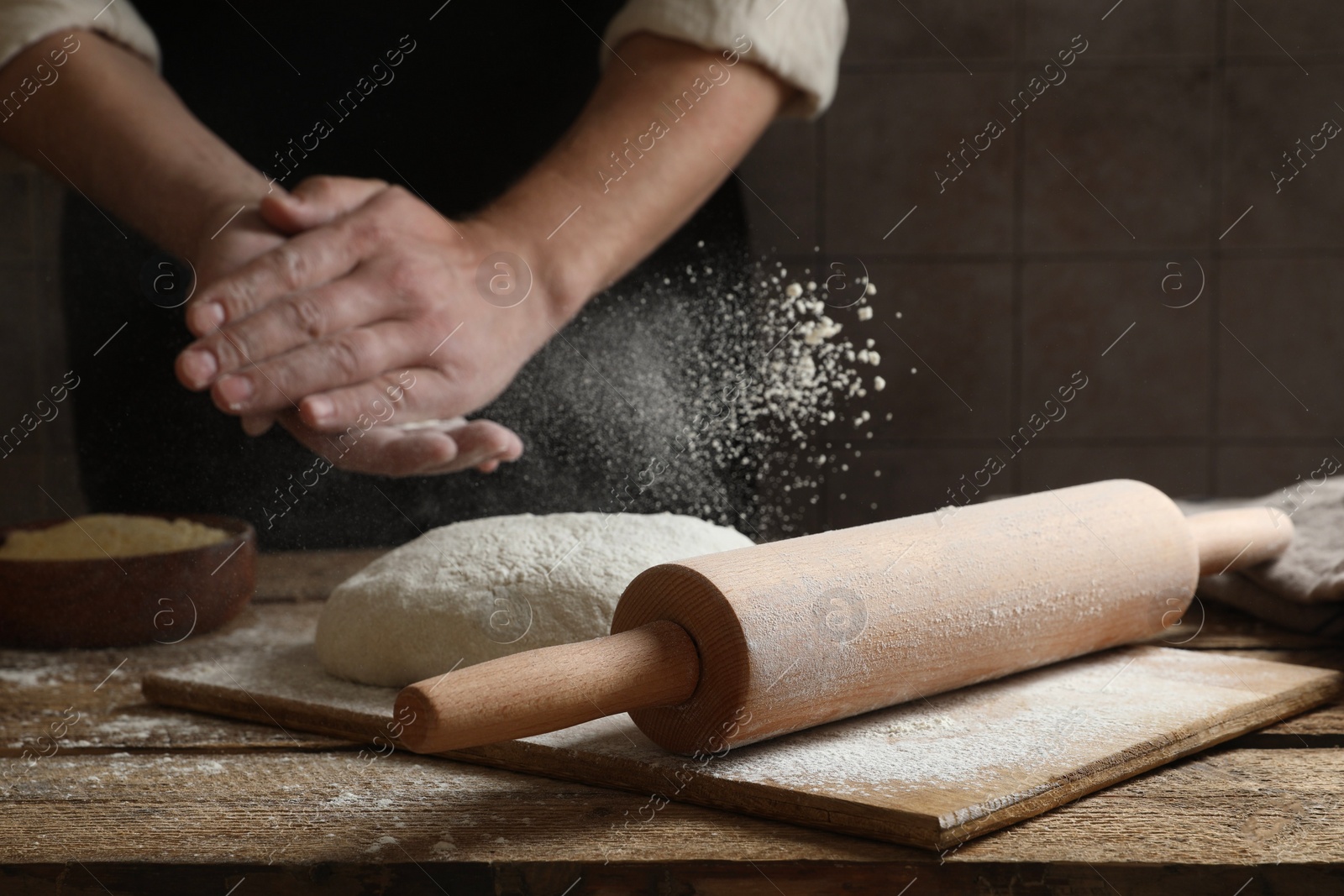 Photo of Man sprinkling flour over dough at wooden table, closeup