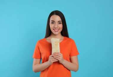 Happy young woman holding tasty shawarma on turquoise background