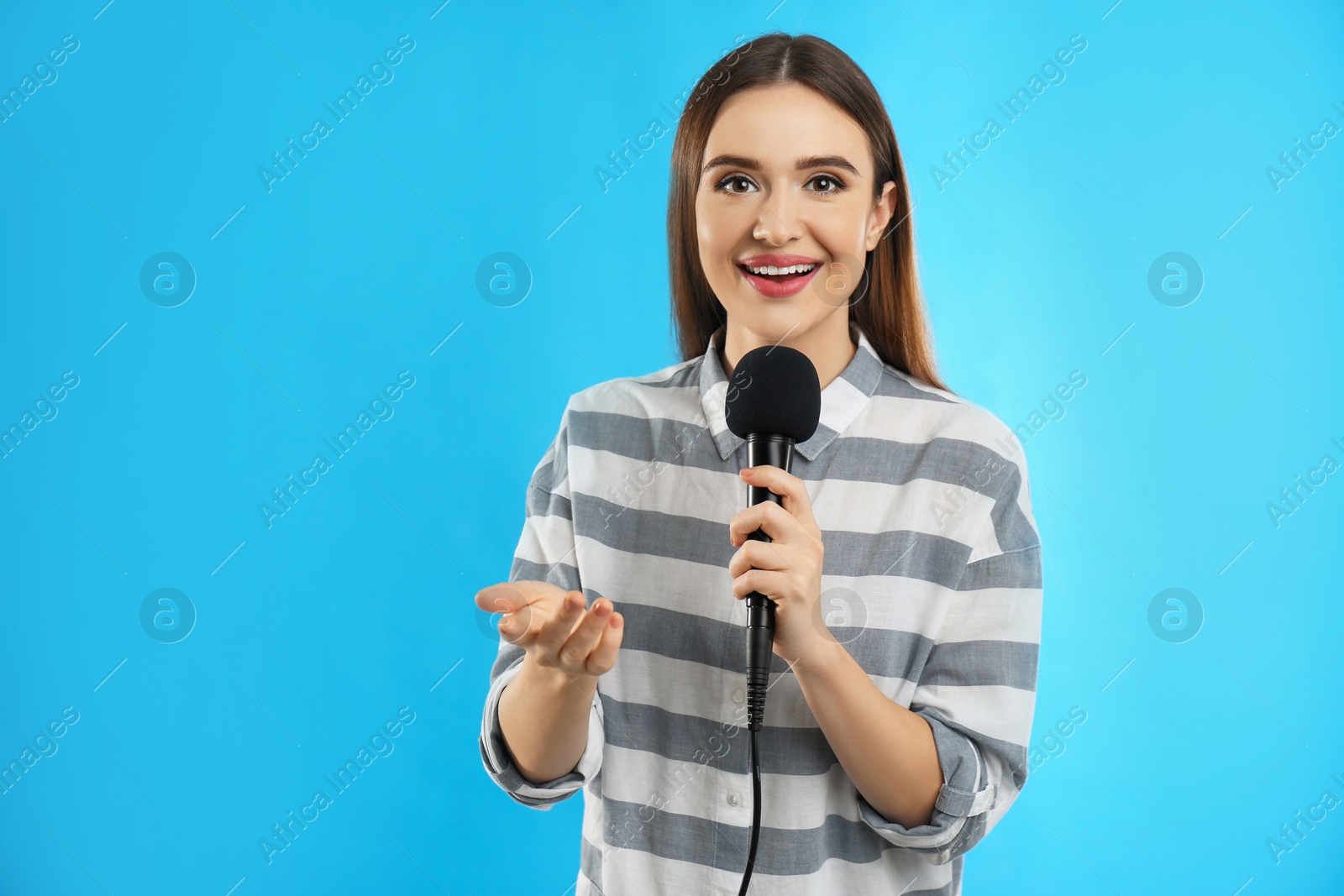 Photo of Young female journalist with microphone on blue background